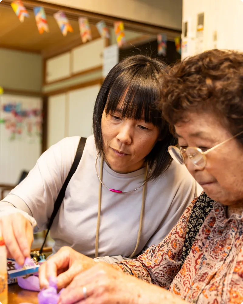 高齢女性の手元を優しく見守りながら作業をサポートする介護ヘルパー