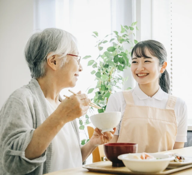 高齢女性の食事介助をしながら笑顔で見守る介護スタッフ