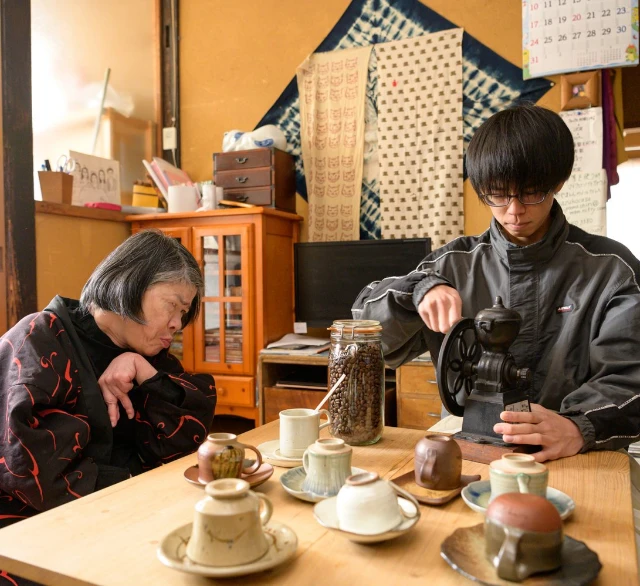 利用者の前で手動の手挽きコーヒーミルで豆を挽く介護スタッフ
