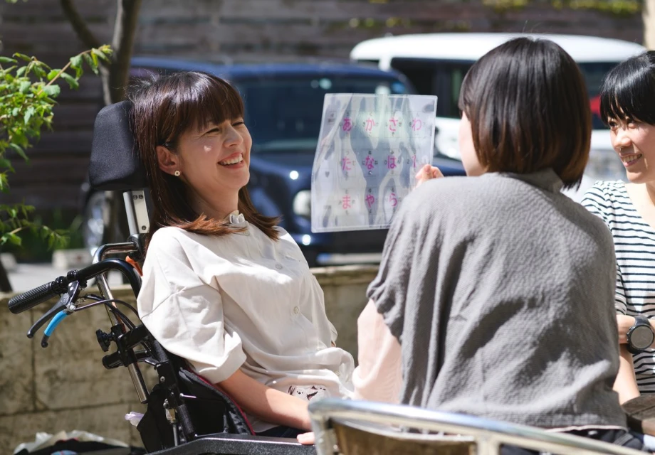 透明な五十音コミュニケーションボードを使って会話を楽しむ車椅子の女性