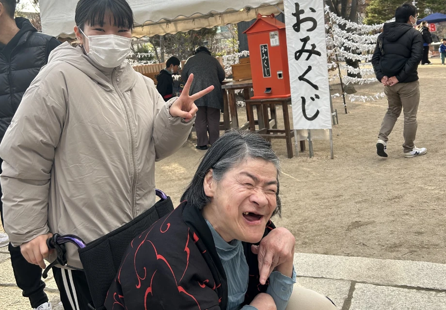 初詣の神社で車椅子の利用者と笑顔で記念撮影をする介護スタッフ