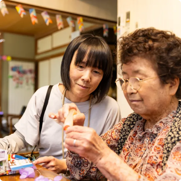 高齢女性の手元を見守りサポートするスタッフ