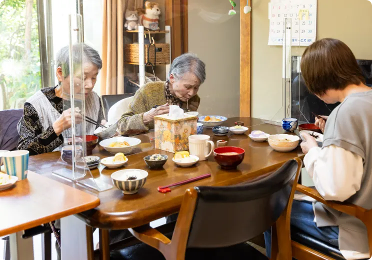 アクリル板を設置した日当たりの良いテーブルで食事を楽しむ利用者