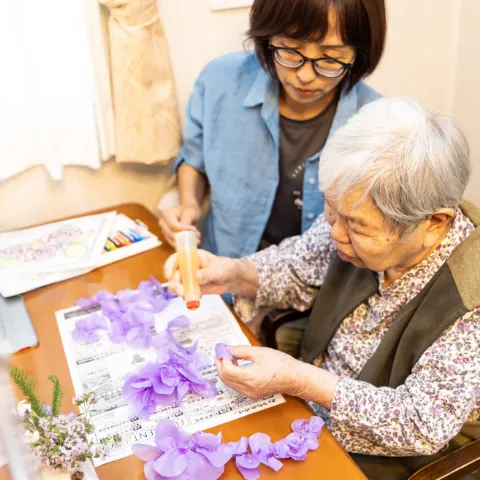 スタッフと一緒に紫の花の工作を楽しむ高齢女性