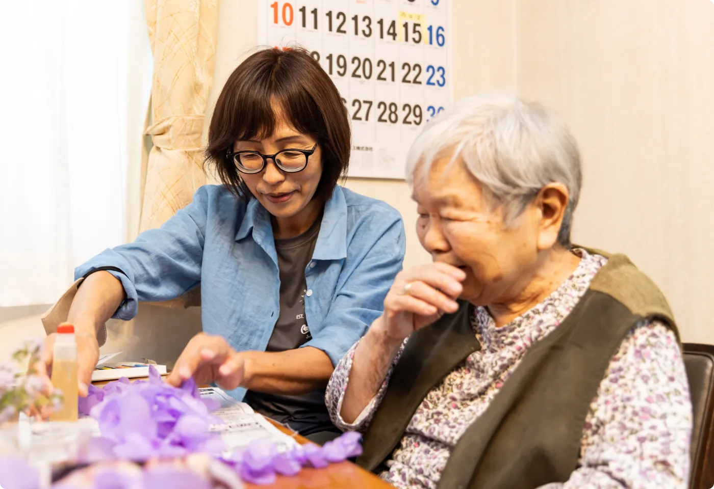 高齢女性と一緒に紫の花の工作を楽しむ介護スタッフ