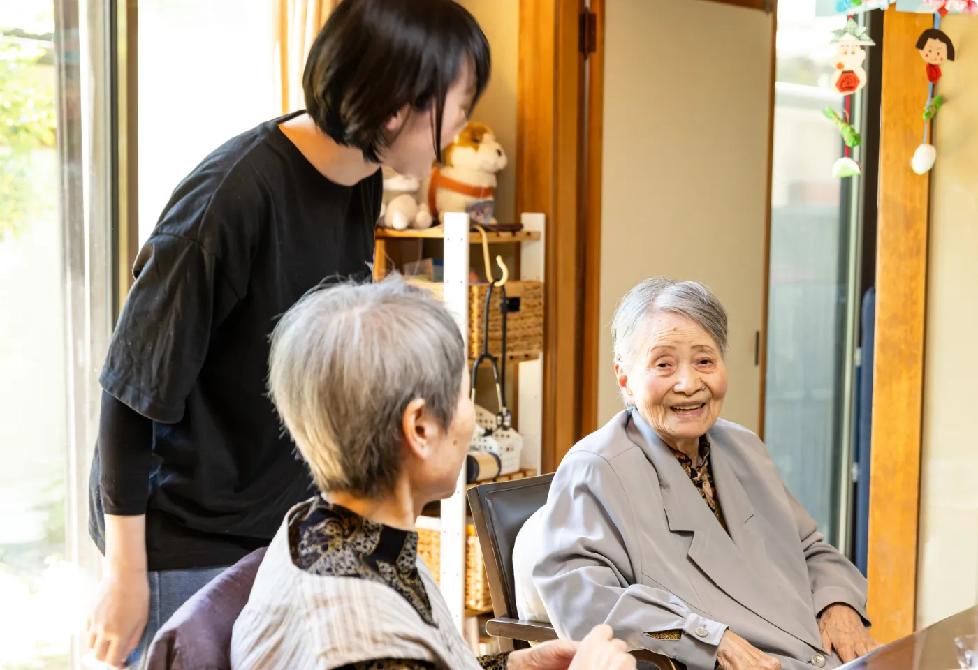 居間で利用者の高齢女性たちと優しく対話する介護スタッフ