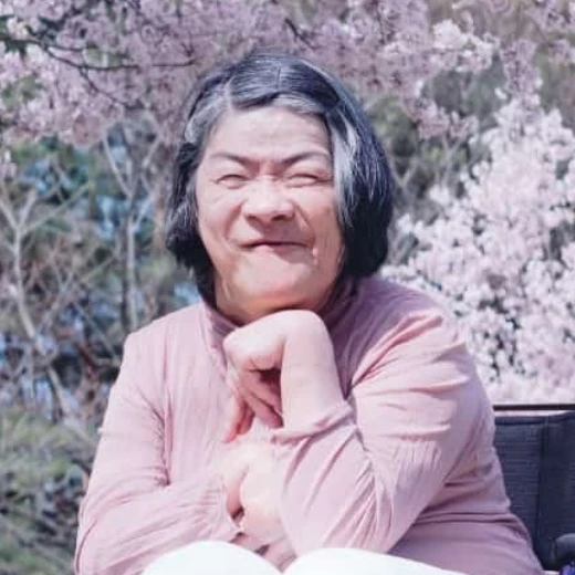 満開の桜をバックに車椅子で笑顔を見せる高齢女性