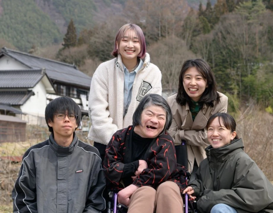 屋外で車椅子の利用者を中心に笑顔で集まる介護スタッフ一同