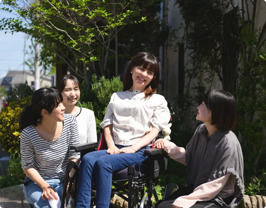 日差しが差し込む屋外で車椅子の女性と和やかに談笑する介護ヘルパーたち
