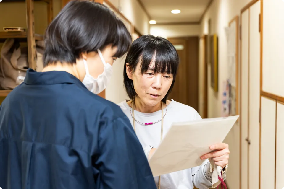 廊下で 書類を確認しながら打ち合わせをする介護スタッフ