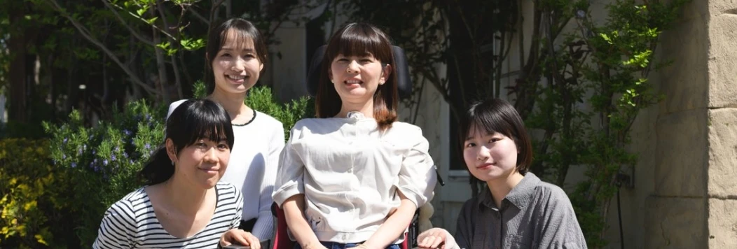 緑豊かな屋外で車椅子の女性を囲んで笑顔で並ぶスタッフたちの記念写真