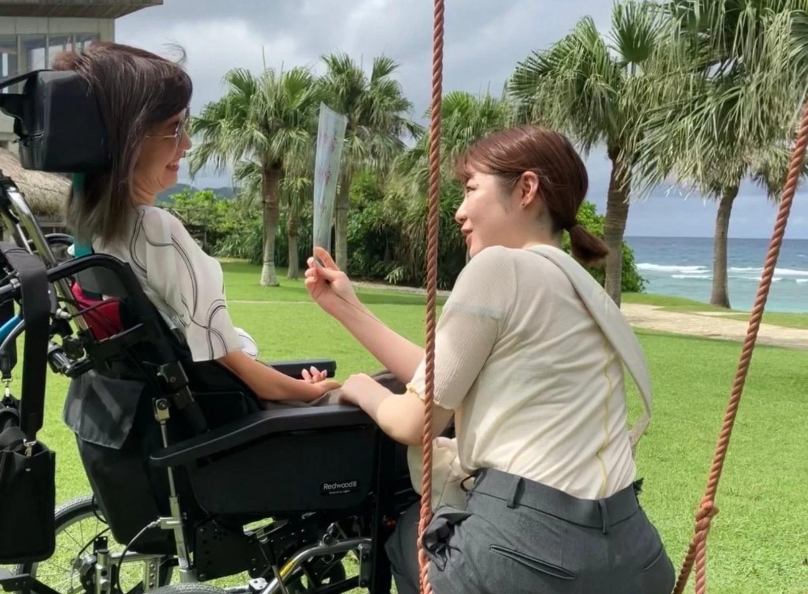 海辺のブランコで車椅子の女性と歓談する介護